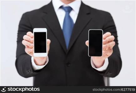 business, internet and technology concept - businessman showing two smartphones with blank black screens