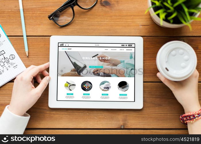 business, internet shopping, technology and people concept - close up of woman with online shop web page on tablet pc computer screen, notebook and coffee on wooden table