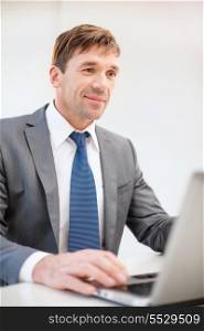 business, internet, technology and office concept - smiling businessman with laptop computer in office