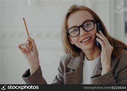 Business lady has telephone call and points with pencil. Elegant happy mid adult businesswoman is working from home. Attractive emotional european lady in jacket is freelancer or entrepreneur.. Business lady has telephone call and points with pencil. Elegant happy mid adult businesswoman.