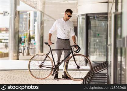 business, lifestyle, transport and people concept - young man parking bicycle on city street. young man parking his bicycle on city street