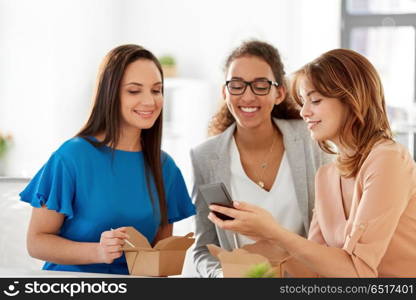 business lunch and people concept - happy businesswomen with smartphone eating take out food at office. businesswomen with smartphone at lunch in office. businesswomen with smartphone at lunch in office