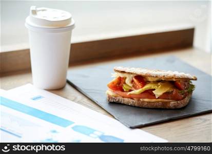 business lunch, food, dinner and eating concept - salmon panini sandwich with tomatoes and cheese, cup of drink and papers on cafe table