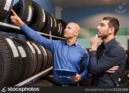 business, maintenance and people concept - male customer and salesman with clipboard showing wheel tires at car repair service or auto store. customer and salesman at car service or auto store