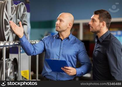 business, maintenance and people concept - male customer and salesman with clipboard showing alloy wheel rims at car repair service or auto store. customer and salesman at car service or auto store