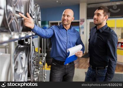business, maintenance and people concept - male customer and salesman with clipboard showing alloy wheel rims at car repair service or auto store. customer and salesman at car service or auto store