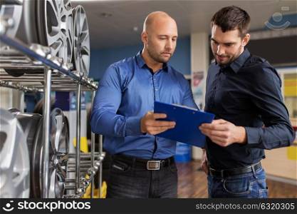 business, maintenance and people concept - male customer choosing alloy wheel rims and salesman with clipboard at car repair service or auto store. customer and salesman at car service or auto store