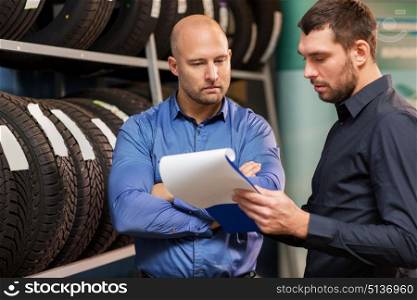 business, maintenance and people concept - male customer choosing wheel discs and salesman with clipboard at car repair service or auto store. customer and salesman at car service or auto store