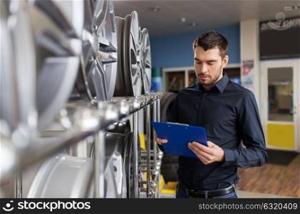 business, maintenance and people concept - male manager with alloy wheel rims and clipboard at car repair service or auto store. auto business owner and wheel rims at car service