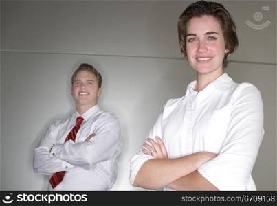 Business man and business woman cross their arms and stand next to each other as they look at the camera