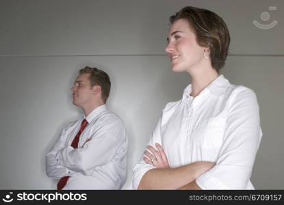 Business man and business woman stand and cross their arms as they look away from the camera