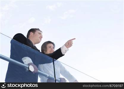 Business man and business woman stand over railing as business man points out