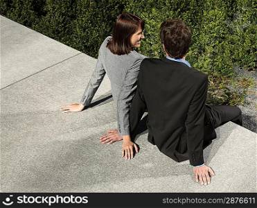 Business man and woman sitting on wall outdoors back view