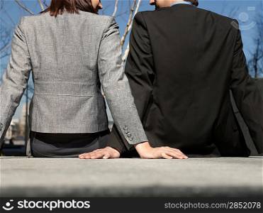 Business man and woman sitting on wall outdoors back view (cropped)