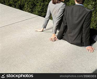 Business man and woman sitting on wall outdoors back view (cropped)