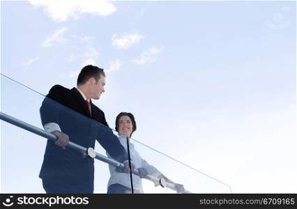 Business man and woman smile as they stand over the rail