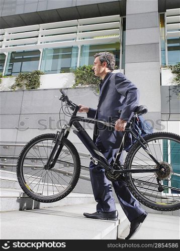 Business man carrying bicycle up steps side view