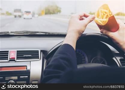 Business man eating french fries and driving car dangerously