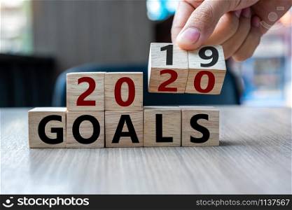 Business man hand holding wooden cube with flip over block 2019 to 2020 Goals word on table background. Resolution, strategy, solution, goal, business and New Year holiday concepts