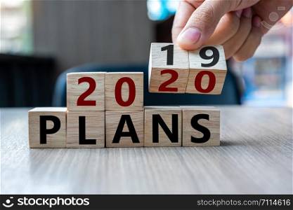 Business man hand holding wooden cube with flip over block 2019 to 2020 Plans word on table background. Resolution, strategy, solution, goal, business and New Year holiday concepts
