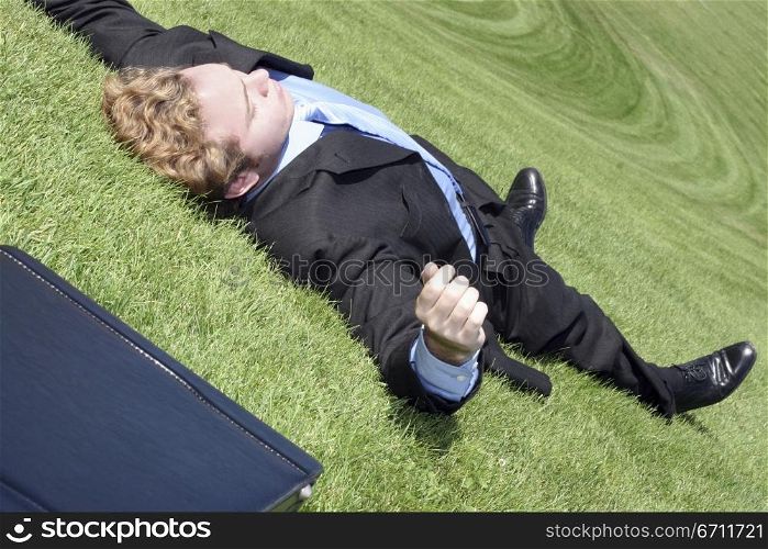 Business man has finally had it, collapses into relaxation on the green hill of tranquility
