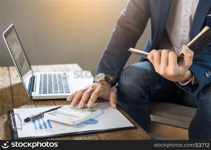 Business man holding a blank notebook and calculate business profits turnover business with calculator in coffee shop or cafe with a laptop computer.