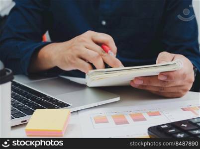 Business man holding pen and book on desk document accounting tax finance graph report investment and marketing with computer laptop.