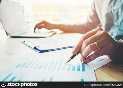 Business man holding pen pointing on summary report chart