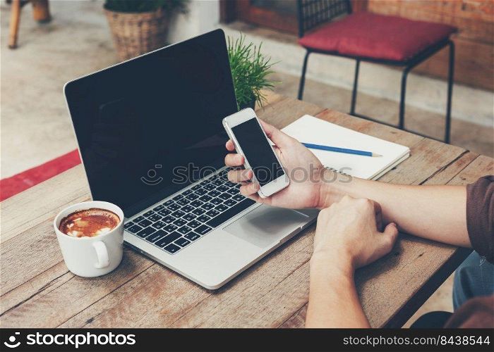 Business man holding phone and laptop on wooden table. Vintage toned.