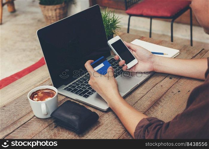 Business man holding phone and payment credit card with laptop on wooden table. Vintage toned.