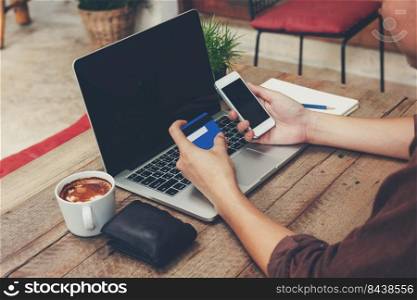 Business man holding phone and payment credit card with laptop on wooden table. Vintage toned.