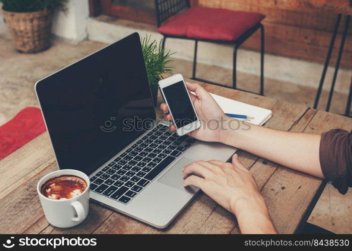 Business man holding phone and using laptop on wooden table. Vintage toned.