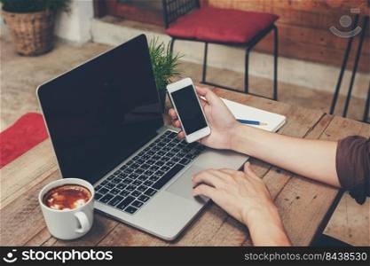 Business man holding phone and using laptop on wooden table. Vintage toned.