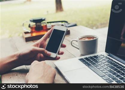 Business man holding phone and using laptop on wooden table. Vintage toned.