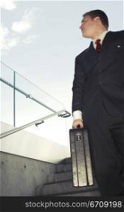 Business man in black suit and red tie smiles as he holds briefcase