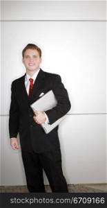 Business man in black suit and red tie standing and holding laptop