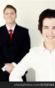 Business man in black suit and tie stands behind smiling woman in white clothes