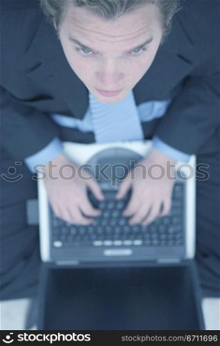 Business man in dark blue suit, blue shirt, and blue tie is typing on his laptop and is looking up