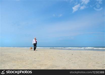 Business man in formal suit walking his dog at the beach