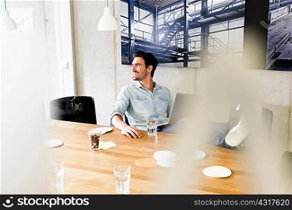 Business man in office feet up on desk, using laptop looking away smiling