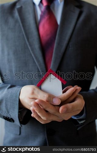 Business man in suit having miniature house on palm of his hand - Business mortgage, property loan, house insurance, business investment concept.