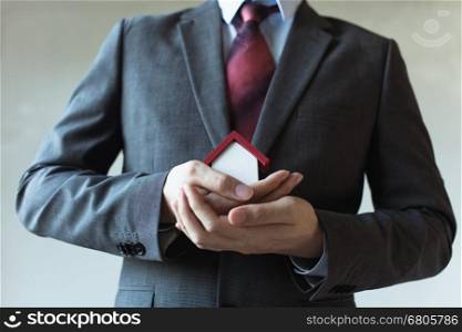 Business man in suit using hands covering and protecting house - Business mortgage, property loan, house insurance, business investment concept.