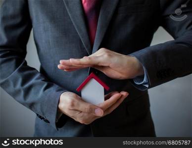 Business man in suit using hands covering and protecting house - Business mortgage, property loan, house insurance, business investment concept.