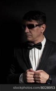 Business man in suit with sunglasses dresses butterfly on a black background