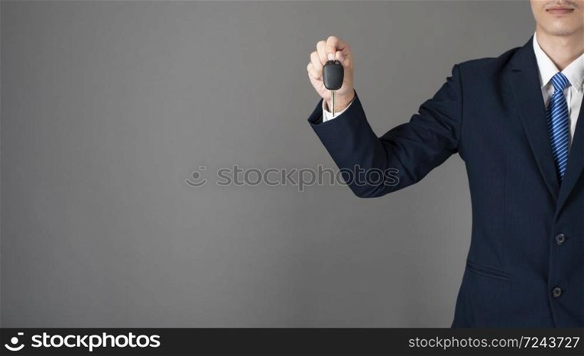 Business man is holding car key, grey background in studio