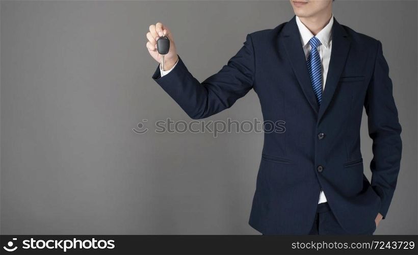 Business man is holding car key, grey background in studio