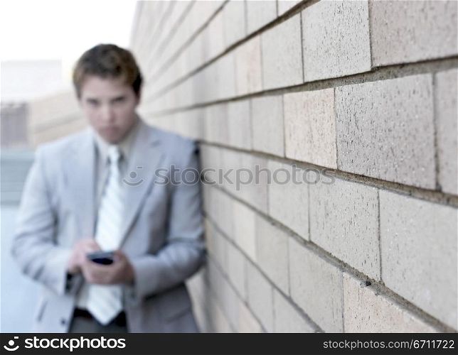 Business man is looking straight at you as he writes on his Pda against a tan brick wall