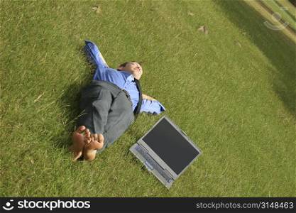 Business man laying barefoot in grass with laptop.