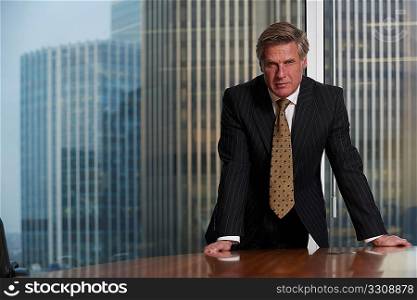 Business man leaning on table in boardroom looking at camera