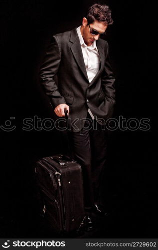 Business man looking down with his luggage on black isolated background